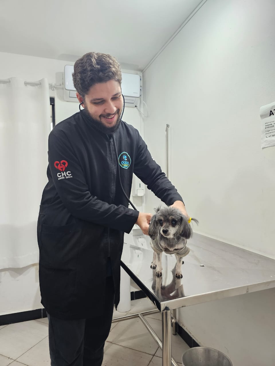 Veterinário com uniforme CHC Saúde Única examinando cão em consultório